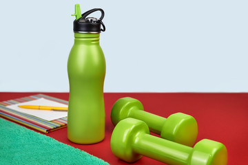 sport, healthy lifestyle and objects concept - close-up of dumbbells, towel, notebook for training...