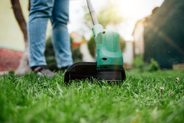 Man cuts grass with electric trimmer.