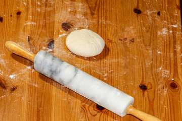 Home Baking. Fresh homemade pizza dough ball on a wooden table sprinkled with flour next to a rolling pin.