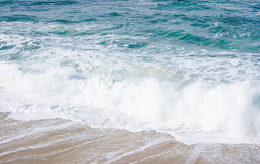 Turquoise ocean water with small white foam waves gently crashing into golden sand beach