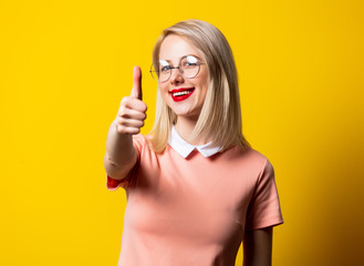 Blonde girl in pink dress show OK gesture on yellow background