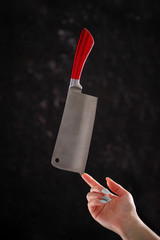 Kitchen ax on a black background with a red handle made of bone. Levitation of a knife on a hand.