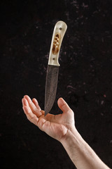 Knife on a black background with a light handle made of bone. Levitation of a knife on a hand.