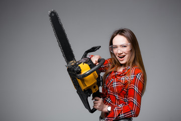 Beautiful sexy girl in red plaid shirt and in transparent glasses holds a chainsaw and crags. Advertising shot for hardware store.