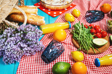 Homemade picnic with fresh fruits, vegetables, salad, orange juice, flowers and baguette on a red plaid. Beautiful still life.
