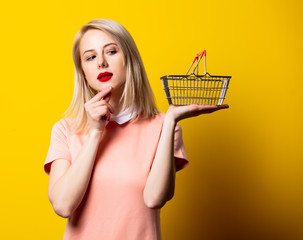 Blonde girl in pink dress with shopping basket on yellow background