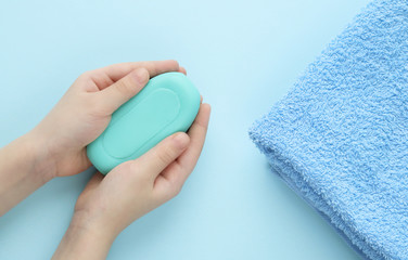 A piece of green soap in the hands of a Caucasian girl and a soft folded towel on a blue background. Selective focus. Care and hygiene of the body and hands. Spa.