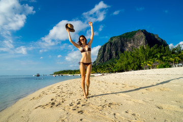 Young girl model posing against a backdrop of picturesque palms, snow-white sand, ocean, boats and mountains. Mauritius Island, Indian Ocean
