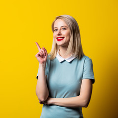 Smiling blonde girl in blue dress on yellow background