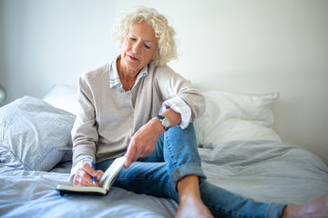 older woman sitting on bed writing in diary