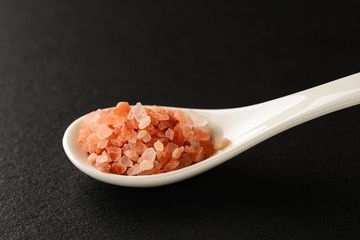 Fototapeta na wymiar Pink himalayan salt in a white chinese porcelain spoon on a black stone serving board. Sauces and seasonings for meat, fish and vegetables.