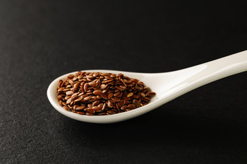 Flax seeds in a white chinese porcelain spoon on a black stone serving board. Sauces and seasonings for meat, fish and vegetables.