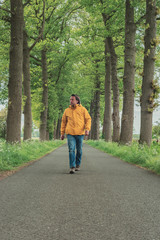 Man in yellow jacket and jeans walks on country road in springtime.