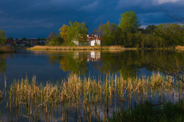 Fototapeta na wymiar Cottage on the lake before the storm, reflection in the water, dark clouds, reeds, water