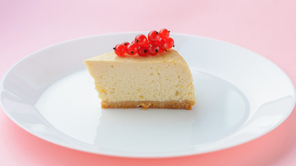 Slice of red currant New York Cheesecake on white plate on pink background