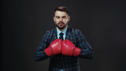 Handsome dramatic young businessman athlete wearing red boxing gloves looking strong face punching at camera training. Strong people. Confidence. Emotions.