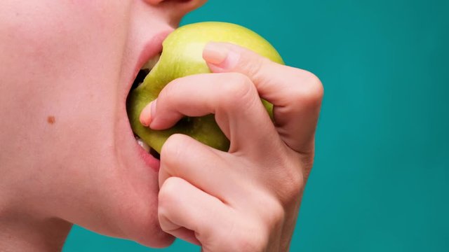 Healthy eating and healthy teeth or diet, young woman bites a fresh apple on a green screen close-up