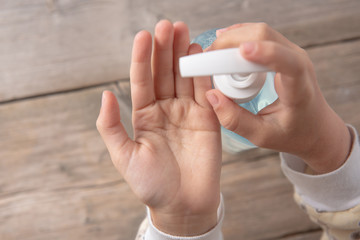 child washes and disinfects hands with an antiseptic on a wooden background. hands in the frame. on the table are liquid soap in the dispenser.