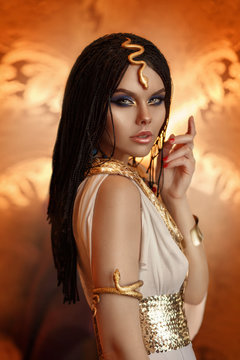 woman queen Cleopatra art photo. Creative golden makeup Black hair braids. Carnival ethnic egypt costume dress. Accessories jewelry snake bracelet crown. Fashion model girl beautiful face close-up