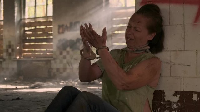 Woman captive chained in handcuffs sitting near wall in abandoned building.