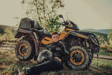 Fototapeta premium portrait of young happy man enjoying beautiful sunny day taking a break from driving a quad,atv in forest