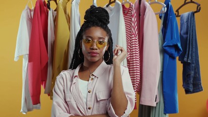 Afro-american attractive woman fashion designer posing at clothes hanger looking at camera. Fashionable girl shopping for trendy clothes sales in shopping mall.