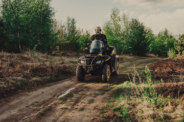 Fototapeta premium A young man in a white helmet rides through the woods on a Quad bike. Extreme hobby. A trip to ATV on the road from logs. Quad Biking through the forest.