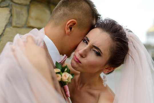 The bride and groom are hugging. Focus on the bride. A woman is looking into the frame. The girl winks. Close-up shot.