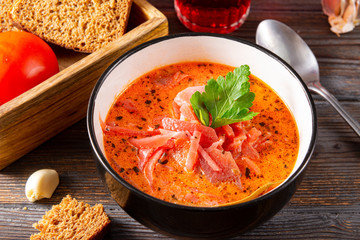 borscht with sour cream and parsley in a  plate,  bread, spoon , garlic on a brown wooden background, red  soup,