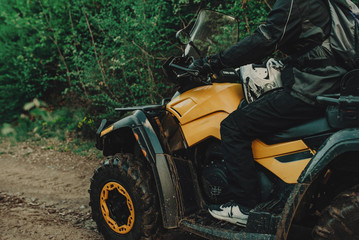 Fototapeta na wymiar A young man in a white helmet rides through the woods on a Quad bike. Extreme hobby. A trip to ATV on the road from logs. Quad Biking through the forest.