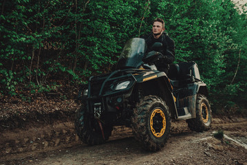 Fototapeta premium A young man in a white helmet rides through the woods on a Quad bike. Extreme hobby. A trip to ATV on the road from logs. Quad Biking through the forest.
