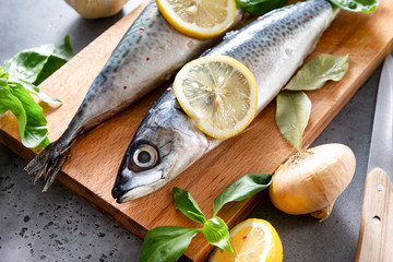 raw mackerel fish with spices and lemon slices on a cutting Board, Basil, garlic, onion, knife on a gray