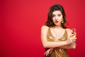 Sexy woman in gold dress with with red lipstick and with champagne in hand over holiday red background. Concept of a New Year holiday, Birthday party