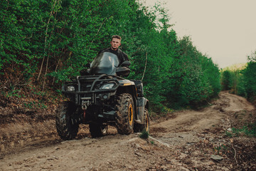 A young man in a white helmet rides through the woods on a Quad bike. Extreme hobby. A trip to ATV on the road from logs. Quad Biking through the forest.