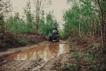 A young man in a white helmet rides through the woods on a Quad bike. Extreme hobby. A trip to ATV on the road from logs. Quad Biking through the forest.