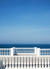 Classic roman white concrete railing outside the building on the terrace or promenade overlooking the sea with blue sky and clouds on the background. Close-up, with copy space.