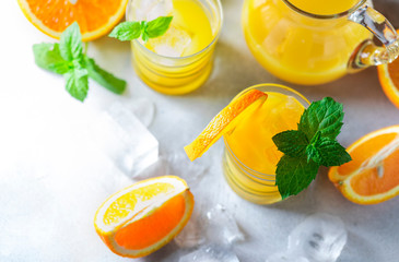 Fresh orange juice, orange slices, mint leaves and ice on a wooden table.