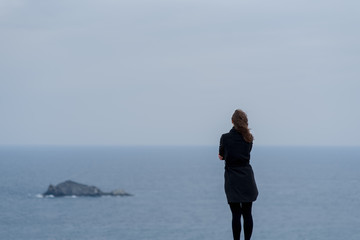 young woman standing against a blue sky and sea 