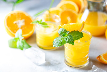 Fresh orange juice, orange slices, mint leaves and ice on a wooden table.