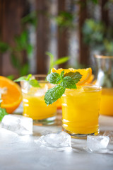 Fresh orange juice, orange slices, mint leaves and ice on a wooden table.