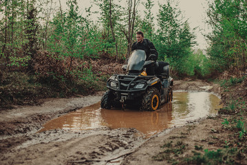 A young man in a white helmet rides through the woods on a Quad bike. Extreme hobby. A trip to ATV on the road from logs. Quad Biking through the forest.