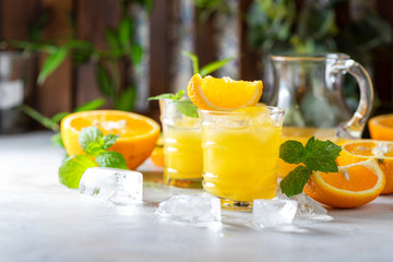 Fresh orange juice, orange slices, mint leaves and ice on a wooden table.