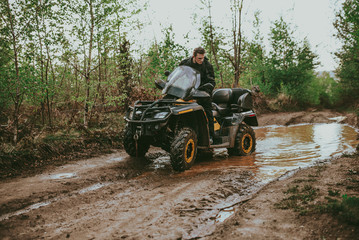 Fototapeta na wymiar A young man in a white helmet rides through the woods on a Quad bike. Extreme hobby. A trip to ATV on the road from logs. Quad Biking through the forest.