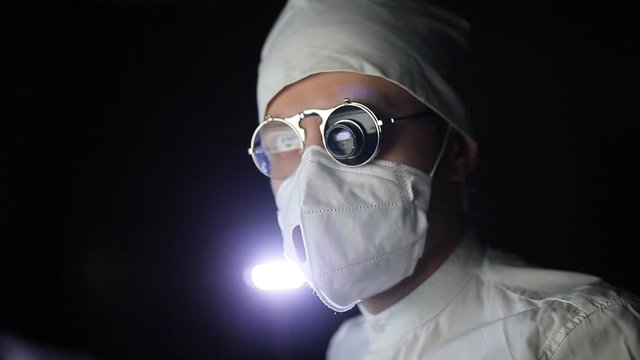 male doctor scientist in a white uniform and glasses with a microscope monocular works in a dark laboratory. secret research.