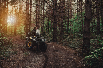 A young man in a white helmet rides through the woods on a Quad bike. Extreme hobby. A trip to ATV on the road from logs. Quad Biking through the forest. © Minet