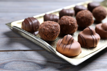 Metal tray with tasty chocolate candies on wooden table, closeup