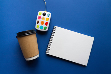 Home office concept. White computer mouse with color dots, spiral notebook and disposable craft cup...