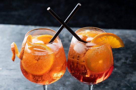 Two glasses of classic italian aperitif aperol spritz cocktail with slice of orange on dark background, traditional summer fresh drink, close up
