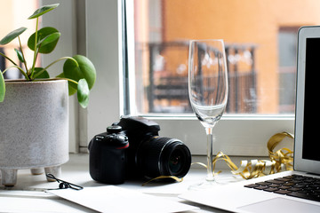 Creative work with an empty champagne glass, camera and laptop while working from home next to the window