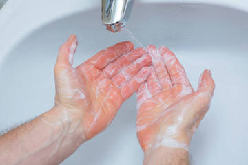 Man washing hands with soap under bathroom sink.
